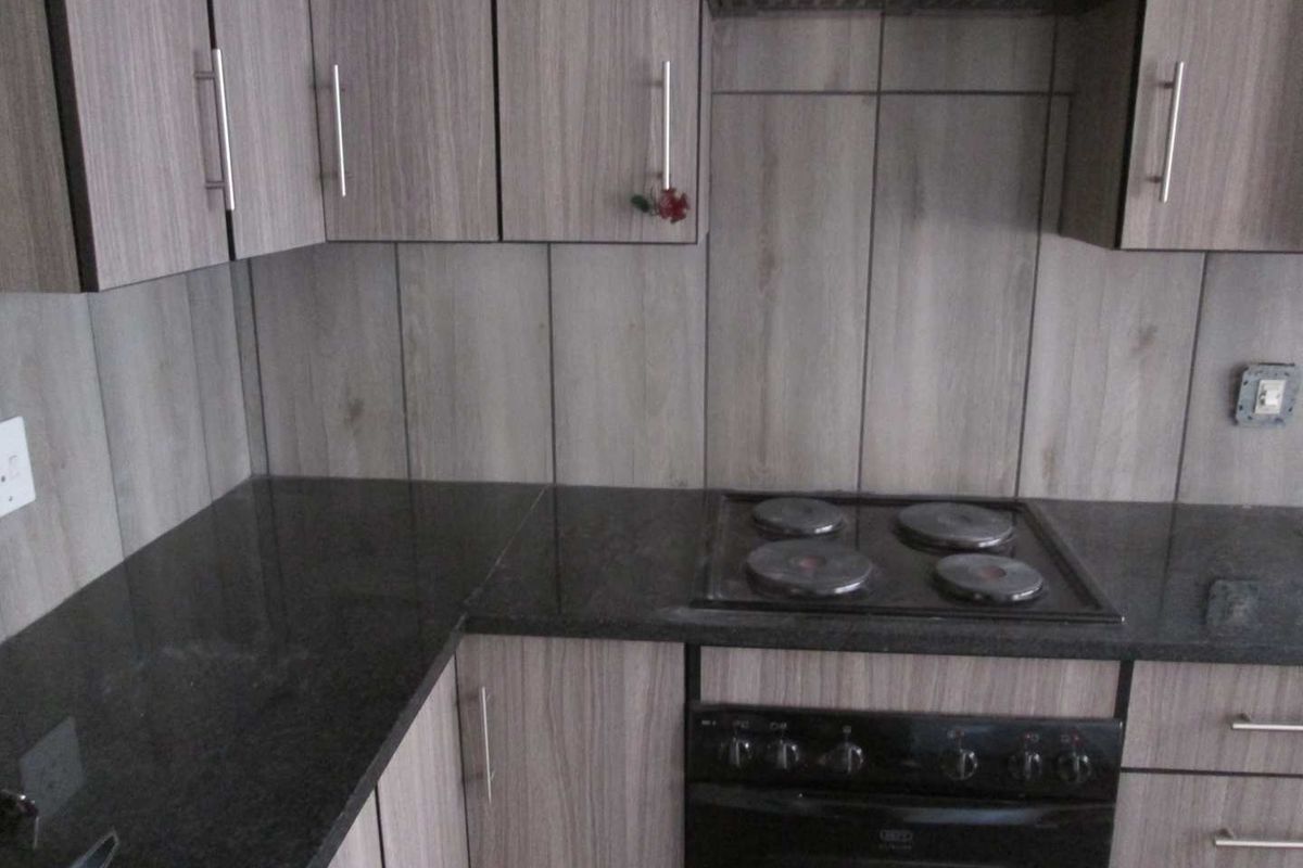 A modern kitchen featuring wood-look laminate cabinetry, dark granite countertops, and a built-in electric oven and hob with a matching extractor fan.