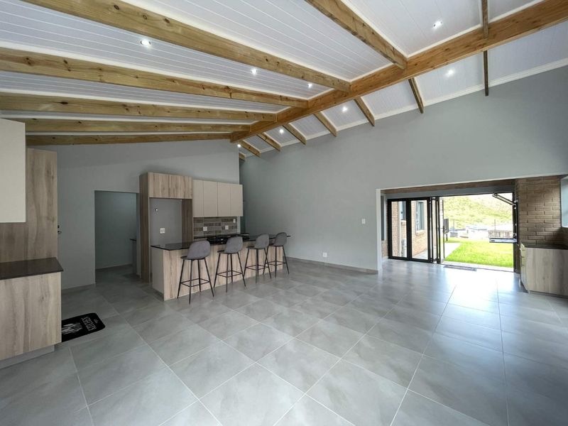 Spacious open-plan living and kitchen area featuring exposed timber ceiling beams, modern tiled flooring, and bi-fold doors opening to the exterior.