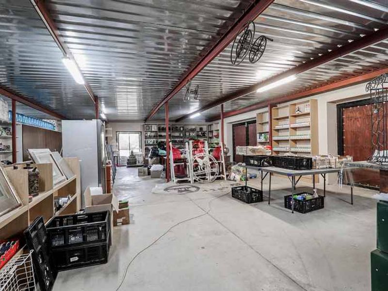A spacious utility area featuring industrial-style corrugated metal ceilings, exposed steel structural beams, concrete flooring, and extensive built-in shelving for storage.