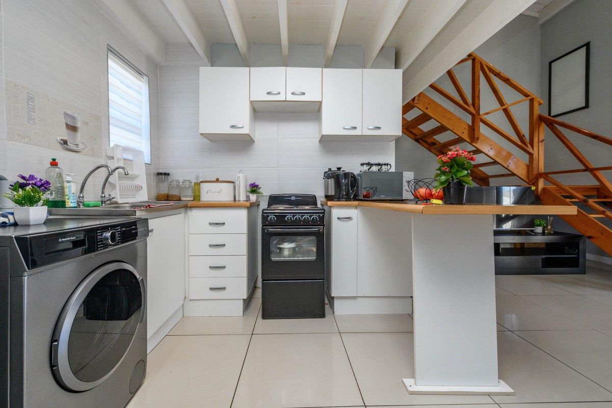 Compact kitchen featuring white cabinetry, wooden countertops, a freestanding oven, and an integrated laundry space, with an adjacent wooden staircase.