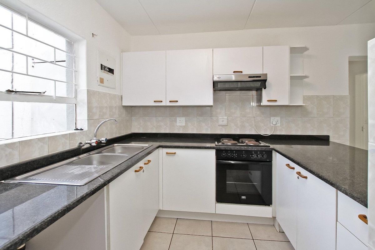 A functional kitchen featuring white cabinetry, dark granite countertops, a built-in oven with hob, and tiled flooring.