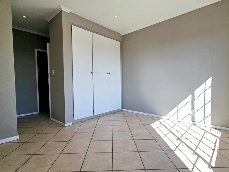 A bright, empty bedroom featuring neutral wall tones, tiled flooring, and built-in storage cupboards.