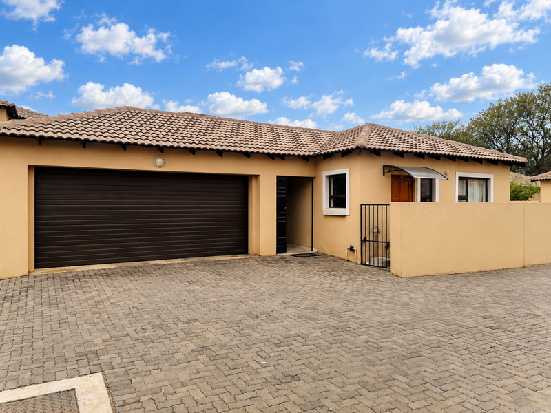 Front elevation of a townhouse featuring a paved driveway, double garage, and secure gated entrance with a tiled roof.