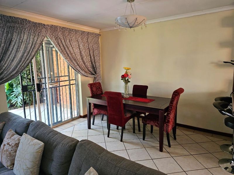 Open plan living and dining area featuring tiled flooring, a sliding glass door with security gate, and a central pendant light fixture.