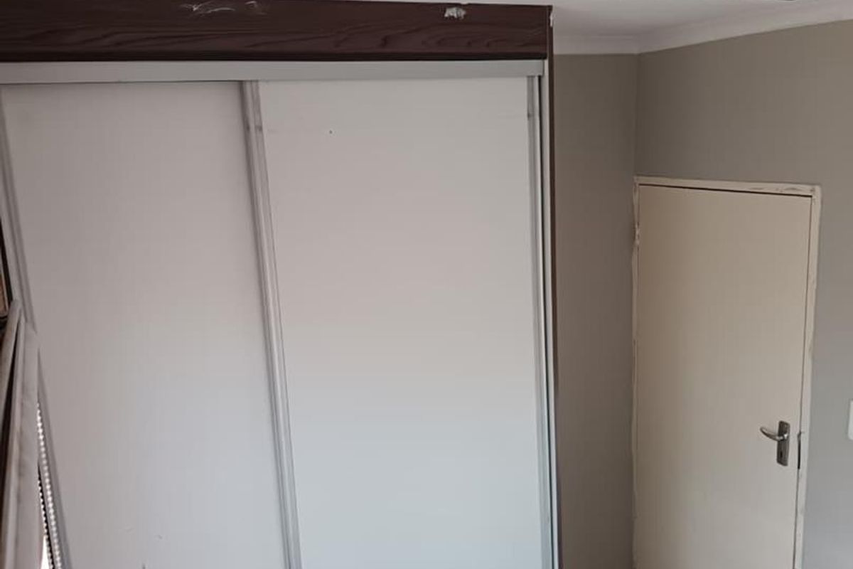 A bedroom featuring a built-in sliding door wardrobe, tiled flooring, and a standard interior door, showing signs of wear on the ceiling and cabinetry.