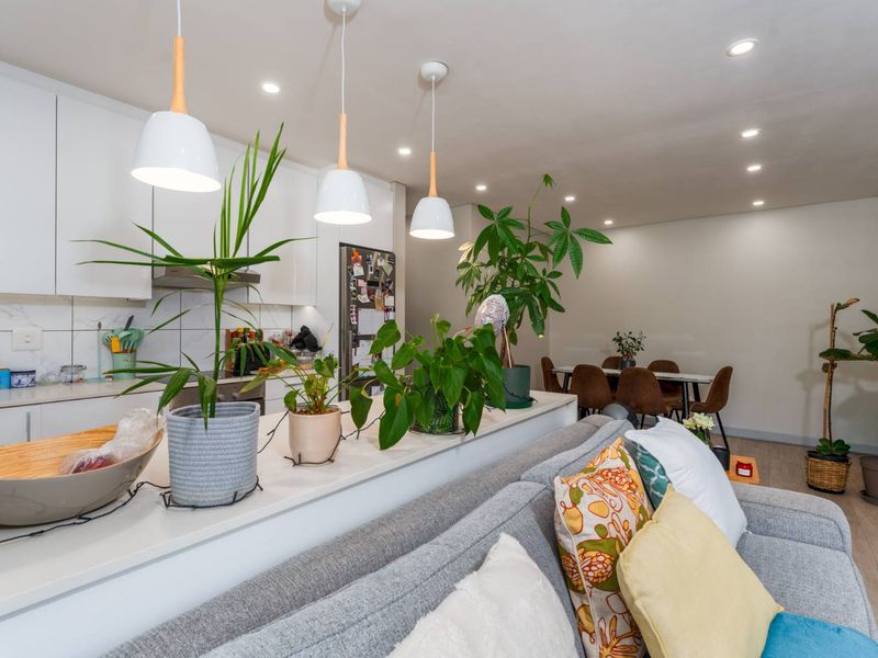 Modern open-plan living area featuring a sleek kitchen with stone countertops, marble-look backsplash, and integrated lighting, flowing into a dining space.
