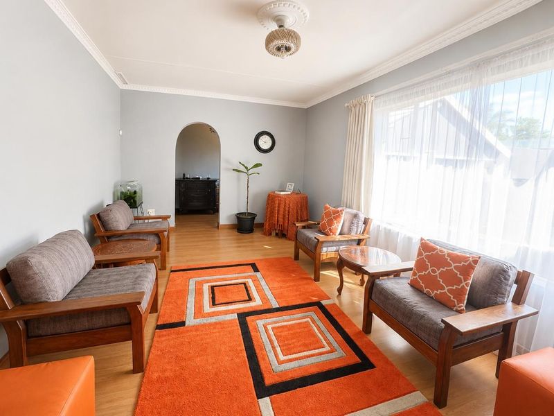 A well-maintained living room featuring laminate flooring, decorative ceiling rose, and a classic arched doorway leading to an adjacent space.