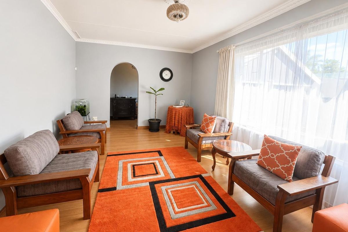A well-maintained living room featuring laminate flooring, decorative ceiling rose, and a classic arched doorway leading to an adjacent space.