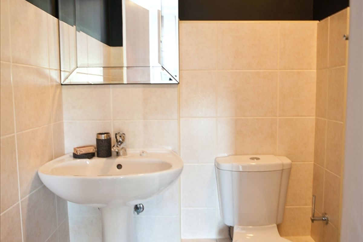 A compact bathroom featuring a white pedestal basin, a standard toilet, and neutral ceramic wall and floor tiling with a contrasting dark upper wall.