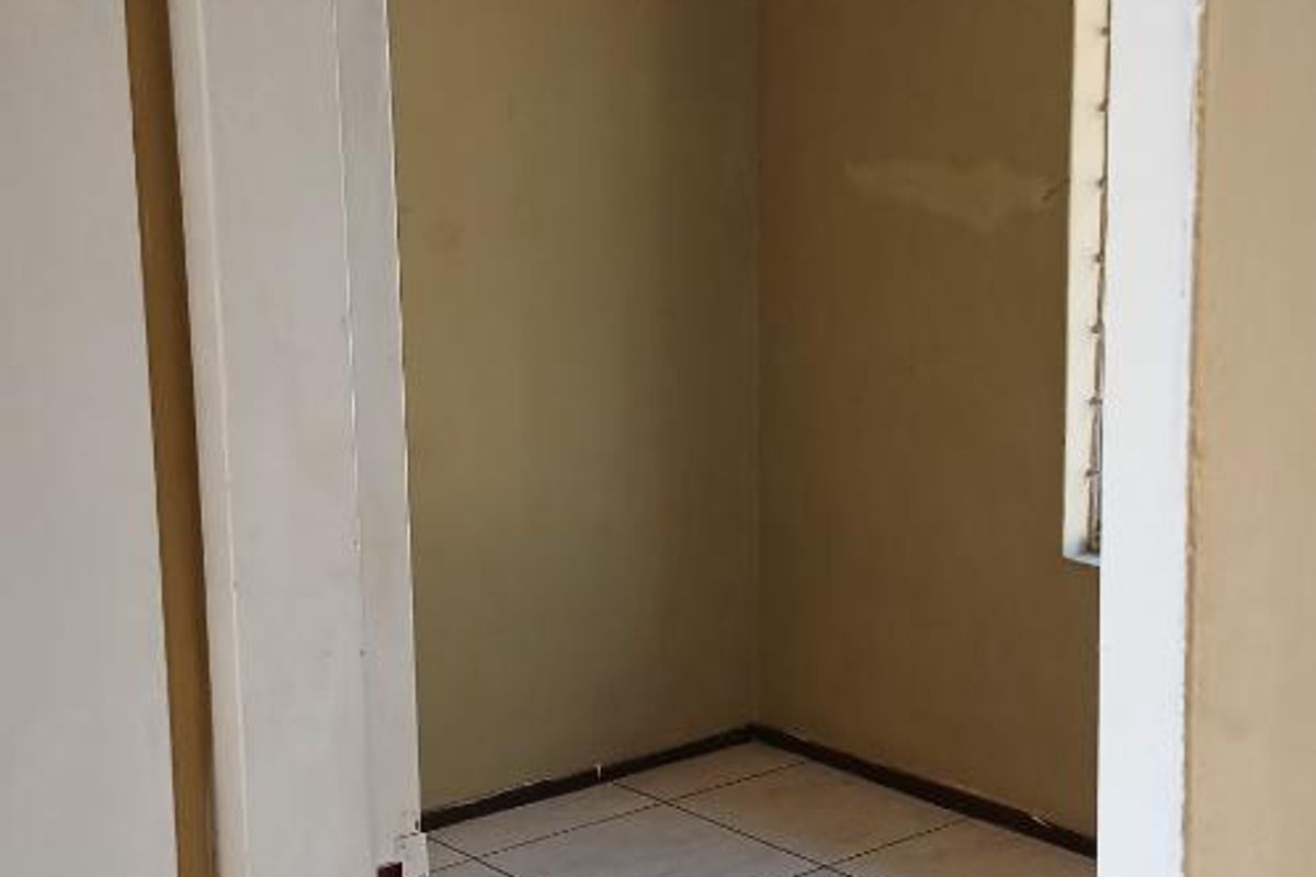 An empty bedroom featuring tiled flooring, a ceiling light fixture, and a louvered window, requiring minor cosmetic updates to the wall finishes.