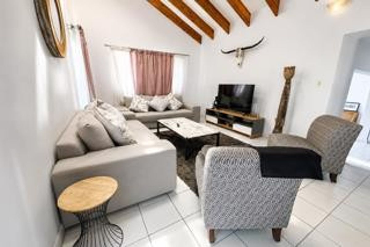 A bright living room featuring a vaulted ceiling with exposed timber beams and tiled flooring, creating a spacious and inviting atmosphere.