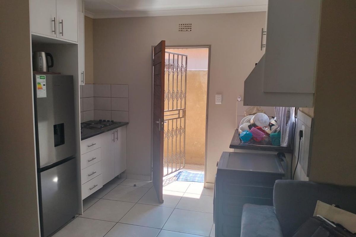 A functional kitchen area featuring built-in cabinetry, a gas hob, and direct access to an exterior space through a security gate.