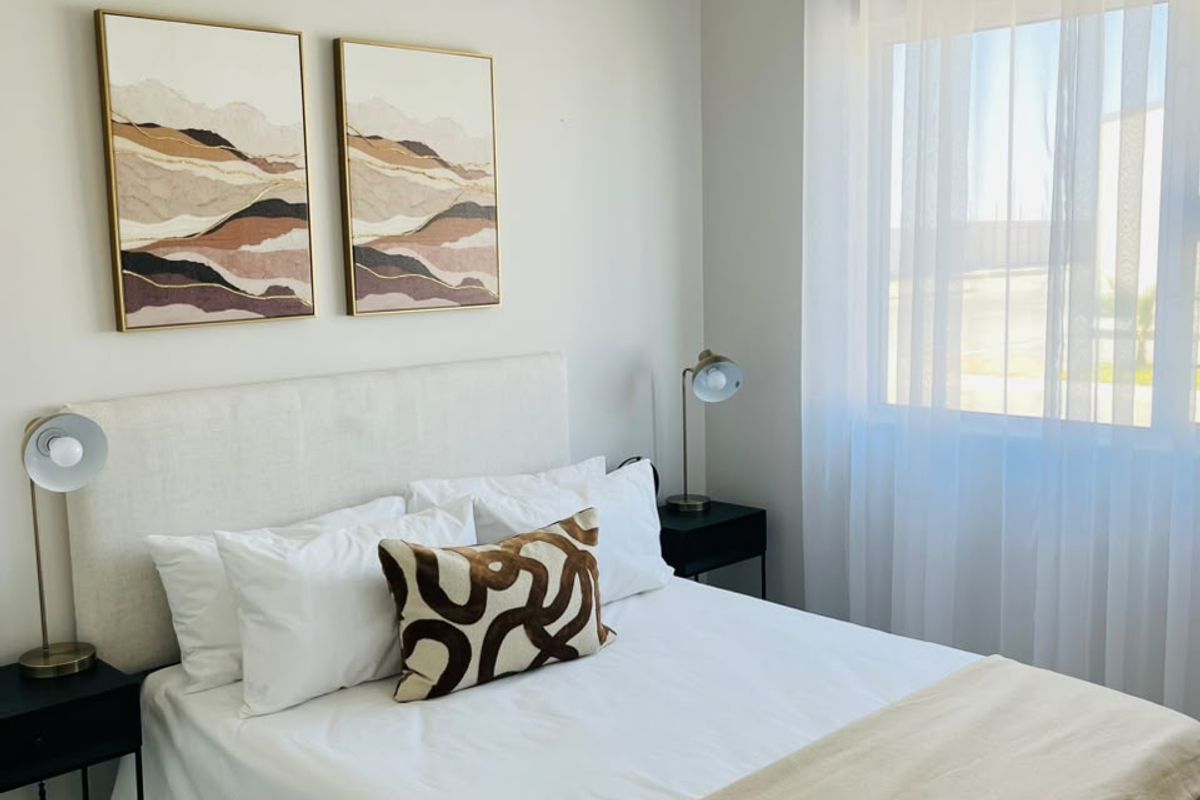 A well-maintained bedroom featuring neutral wall tones, tiled flooring, and a window with a curtain rod, offering a bright and comfortable living space.