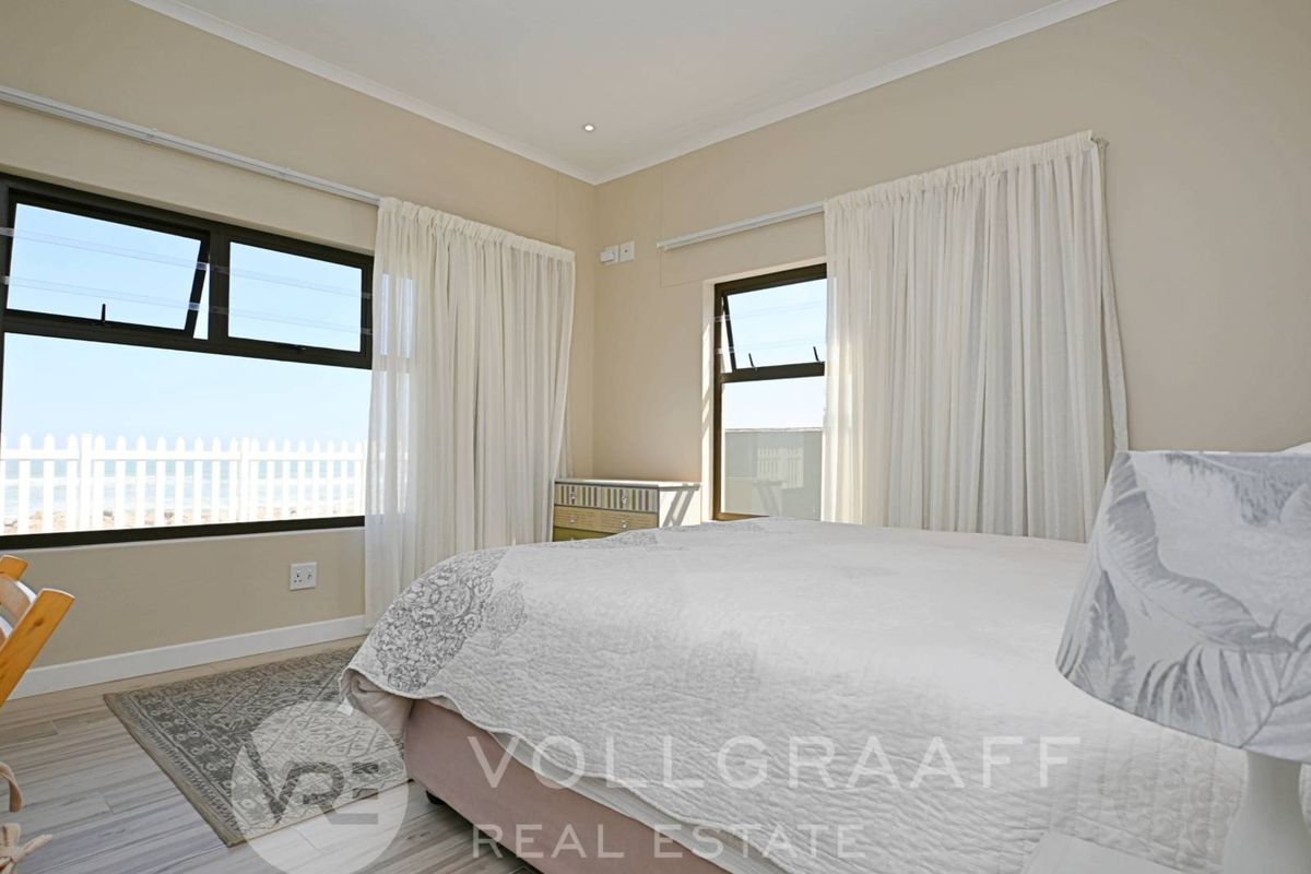 A bright bedroom featuring large windows with views, neutral wall tones, and modern wood-look flooring.
