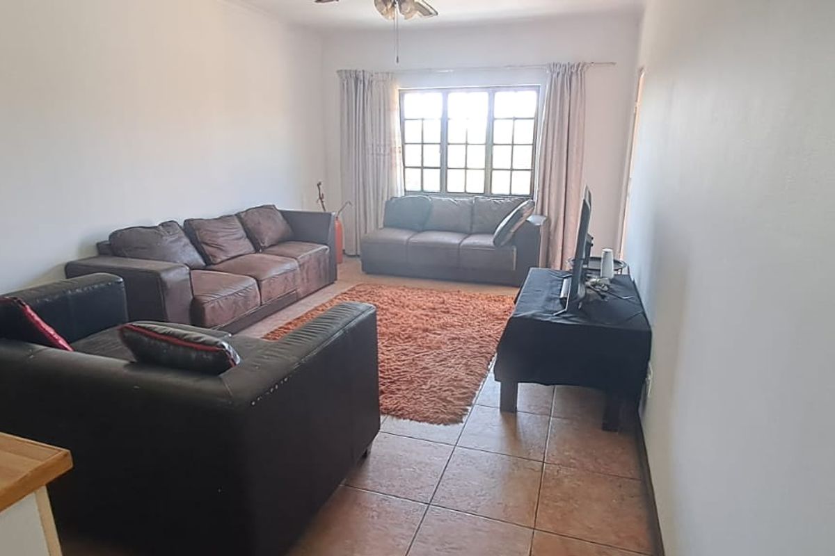A functional living room featuring tiled flooring, a ceiling fan, and a window with security bars, providing a comfortable and practical living space.