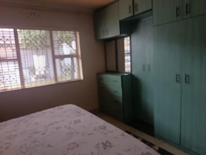 A bedroom featuring built-in cupboards and security bars on the window. The room requires cosmetic updates to modernize the finishes.