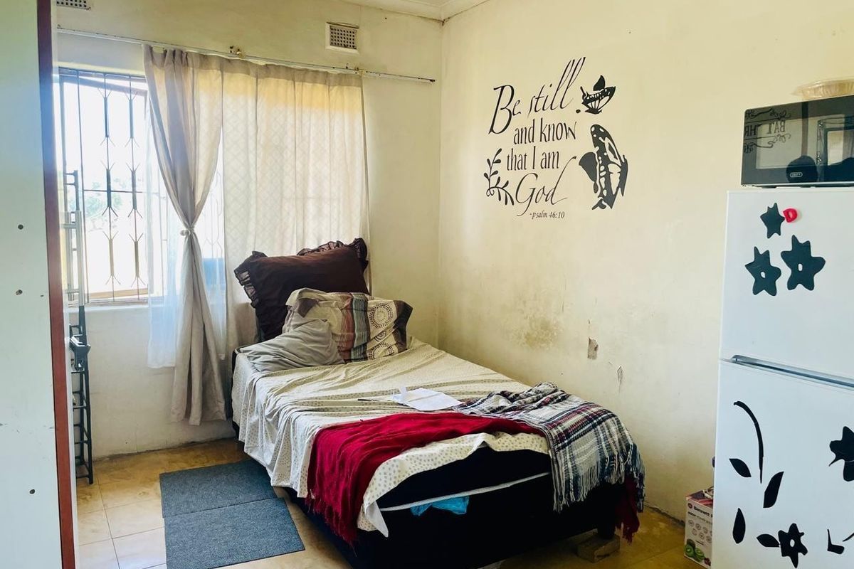 A compact bedroom featuring tiled flooring, security bars on the window, and a ceiling vent, requiring cosmetic updates to the wall finishes.