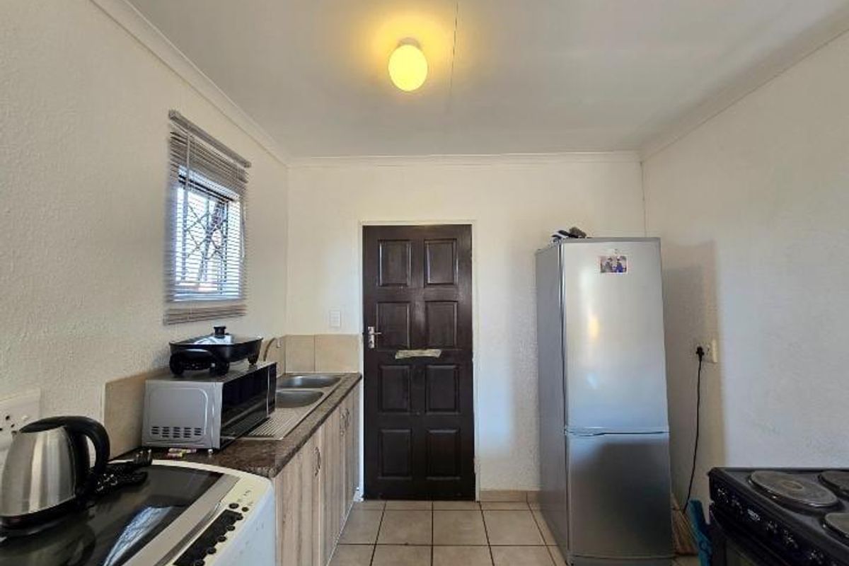 A compact kitchen featuring built-in cabinetry, laminate countertops, a stainless steel sink, and tiled flooring, with a window fitted with security bars.