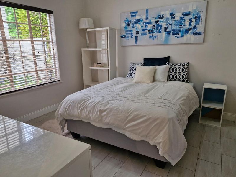 A well-lit bedroom featuring neutral tiled flooring, clean wall finishes, and venetian blinds providing natural light.