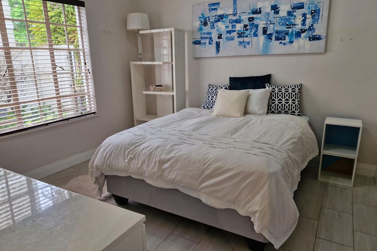 A well-lit bedroom featuring neutral tiled flooring, clean wall finishes, and venetian blinds providing natural light.