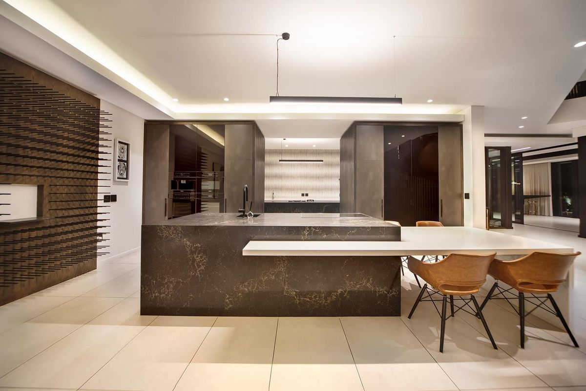 Modern luxury kitchen featuring a large stone island, integrated high-end cabinetry, built-in appliances, and sophisticated recessed and pendant lighting in an open-plan layout.