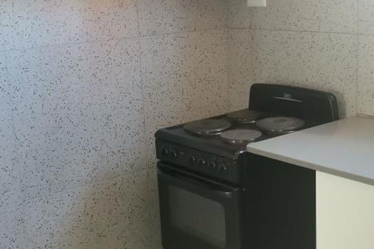 A compact kitchen area featuring tiled walls and flooring, overhead cabinetry, and a freestanding electric stove.