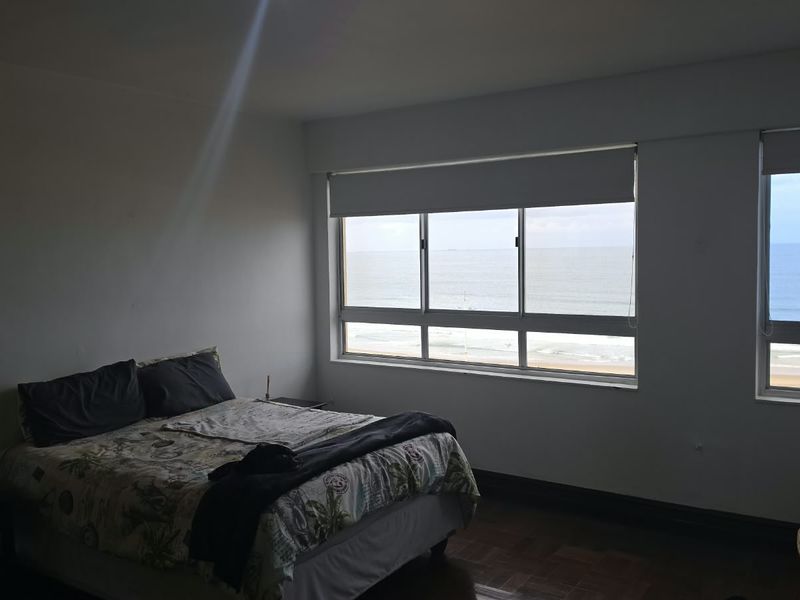 A bedroom featuring parquet flooring and large windows offering expansive ocean views, providing a bright and airy atmosphere.