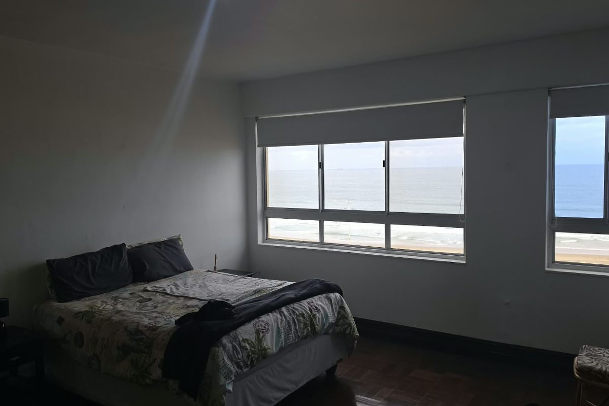 A bedroom featuring parquet flooring and large windows offering expansive ocean views, providing a bright and airy atmosphere.