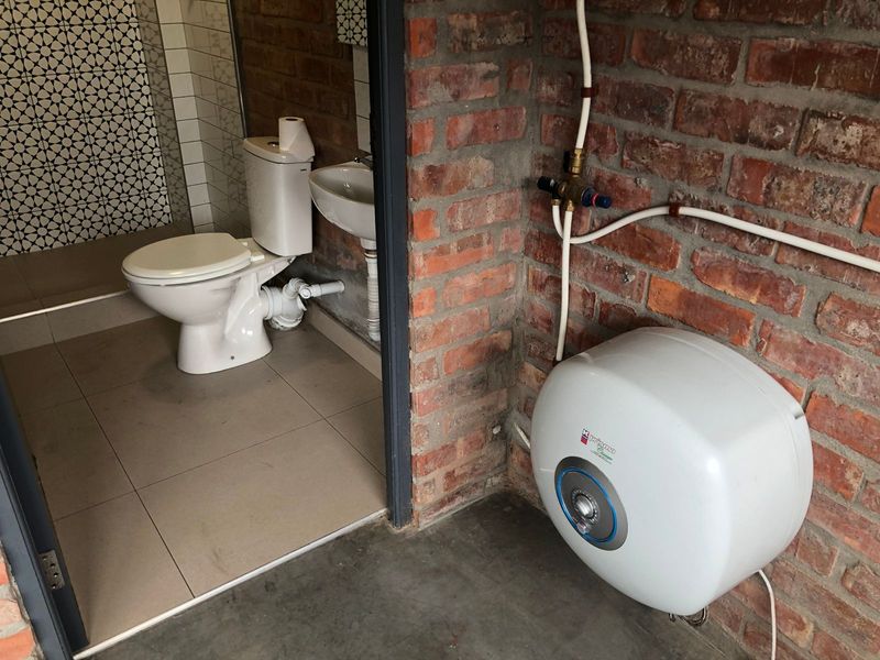A functional bathroom space featuring exposed brick walls, a wall-mounted basin, toilet, and an electric water heater unit.