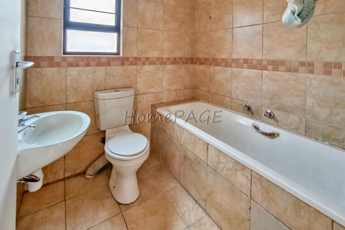A functional bathroom featuring a bathtub, toilet, and wall-mounted basin with neutral floor-to-ceiling tiling and a window for natural light.