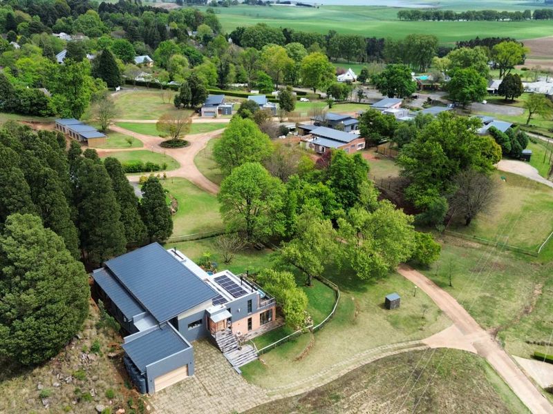 Aerial view of a modern residential property featuring a metal roof, solar panels, and a spacious landscaped garden within a scenic estate setting.