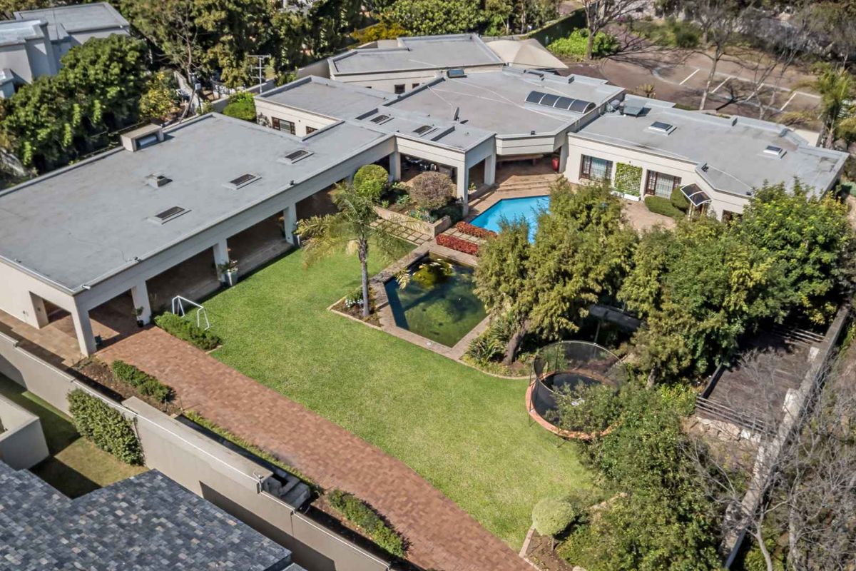 Aerial view of a sprawling residential property featuring a large lawn, swimming pool, decorative pond, and extensive flat roof structure with skylights.