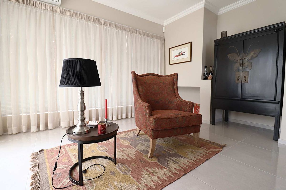 A bright living room featuring neutral tiled flooring, crown molding, and a built-in wall niche, complemented by floor-to-ceiling sheer curtains.