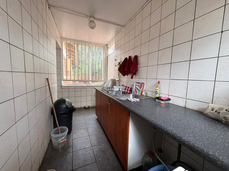 A functional scullery or utility area featuring tiled walls, a stainless steel sink, and built-in cabinetry, providing practical space for wash-up and storage.