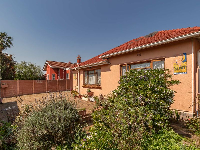 A view of the rear exterior of the house featuring a paved patio area, brick boundary wall, and tiled roof.