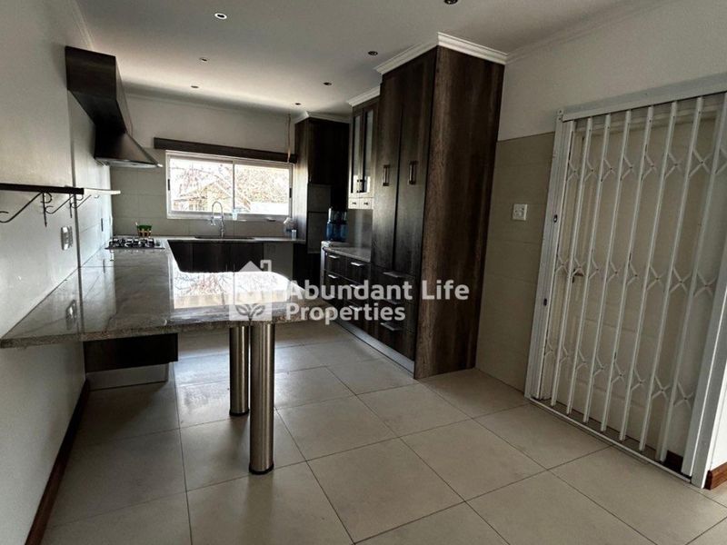 Modern kitchen featuring dark wood cabinetry, granite countertops, a gas hob with extractor, and tiled flooring, offering a clean and functional workspace.