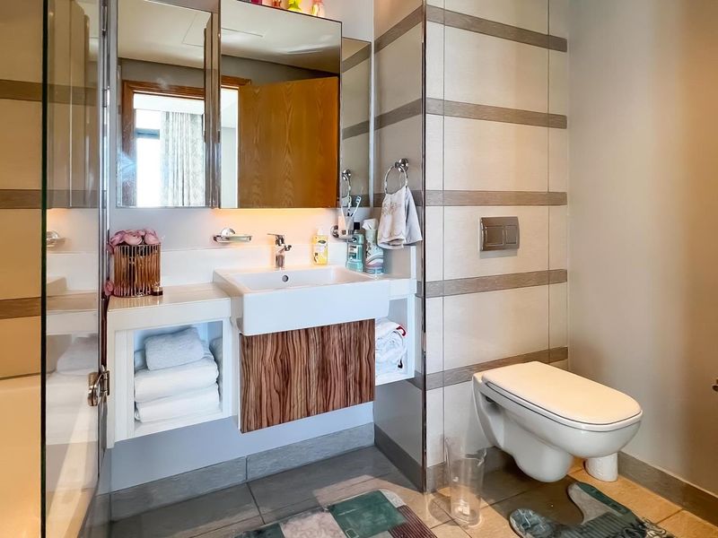 Modern bathroom featuring a wall-mounted toilet, floating vanity with integrated basin, mirrored cabinetry, and a bathtub with glass screen.