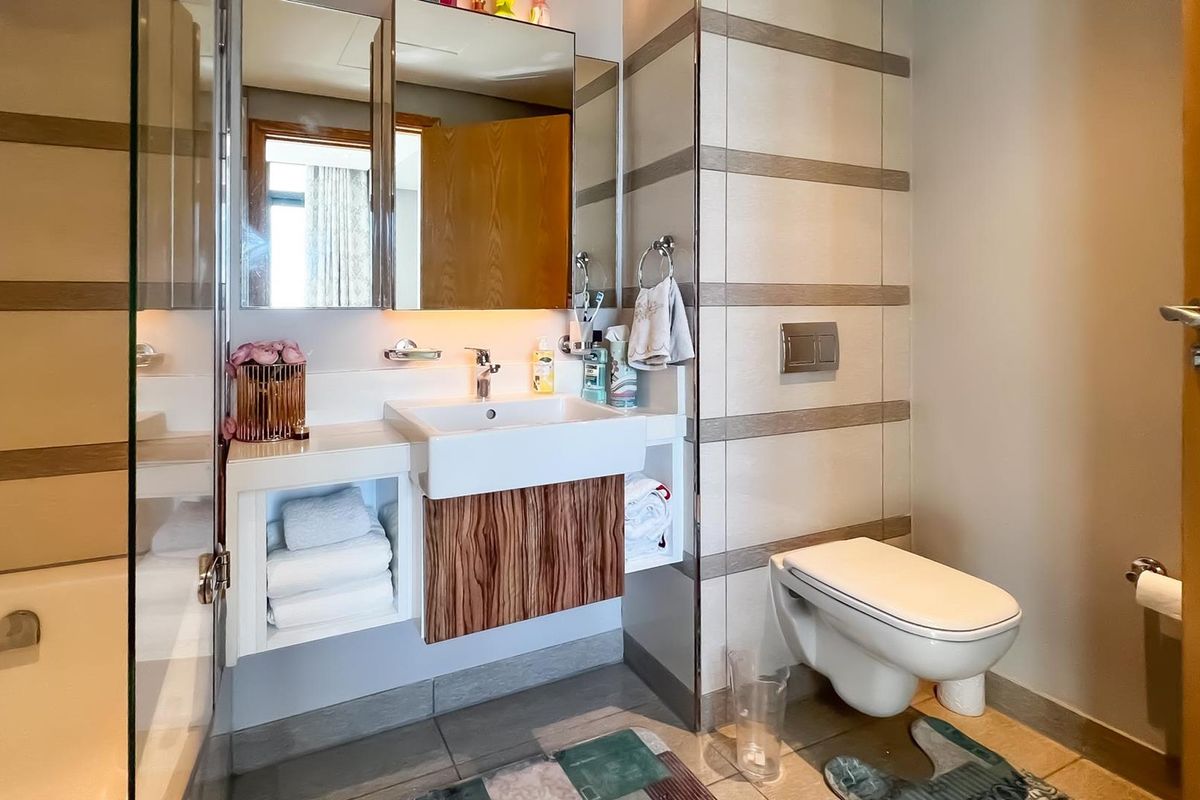 Modern bathroom featuring a wall-mounted toilet, floating vanity with integrated basin, mirrored cabinetry, and a bathtub with glass screen.