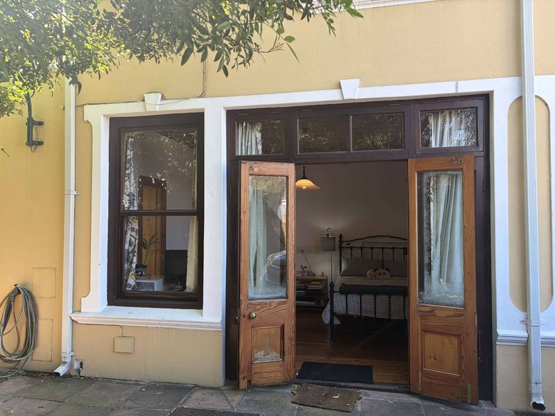 Rear exterior view of an apartment featuring timber-framed double doors and a sash window opening onto a paved patio area.