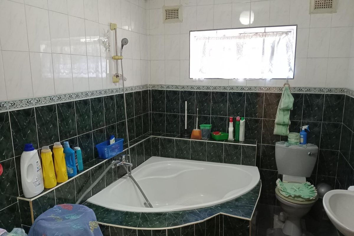 A dated bathroom featuring a corner bathtub, wall-mounted shower head, and toilet, finished with contrasting dark and light wall tiles.