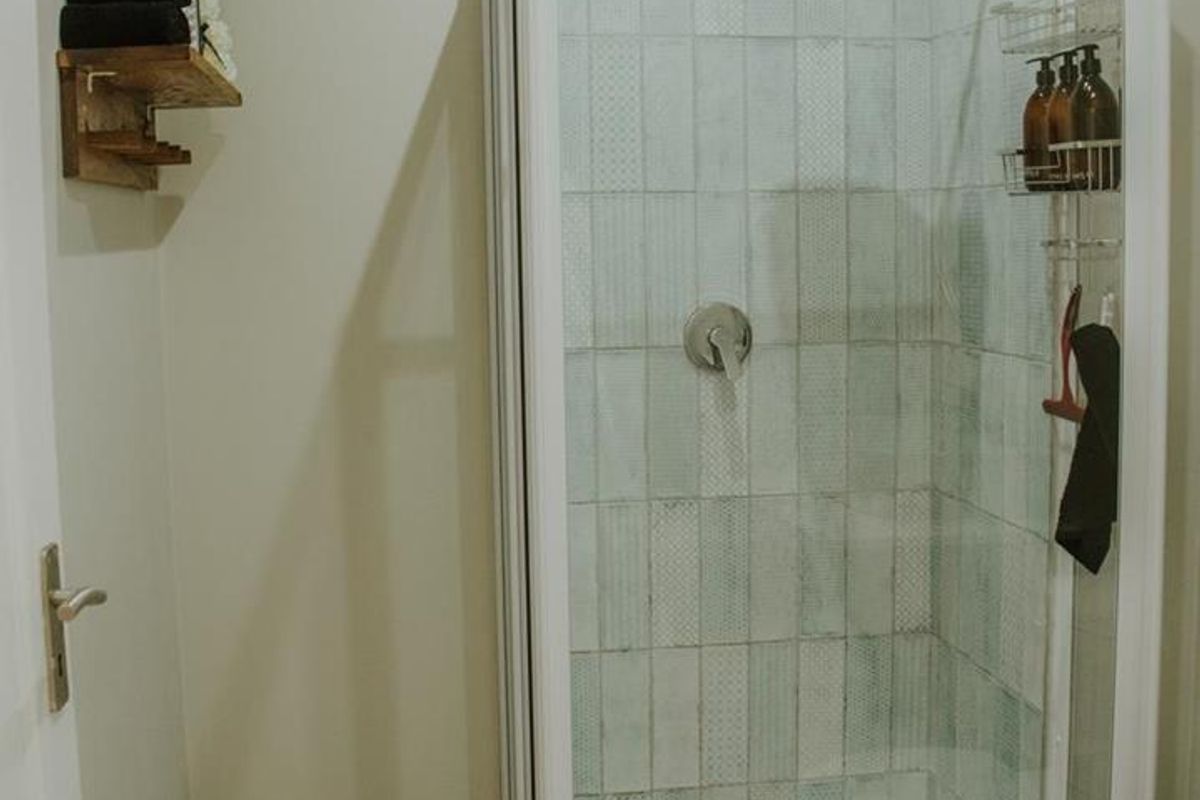 A functional bathroom featuring a glass-enclosed shower with decorative light blue tiling, a rain shower head, and a standard toilet.