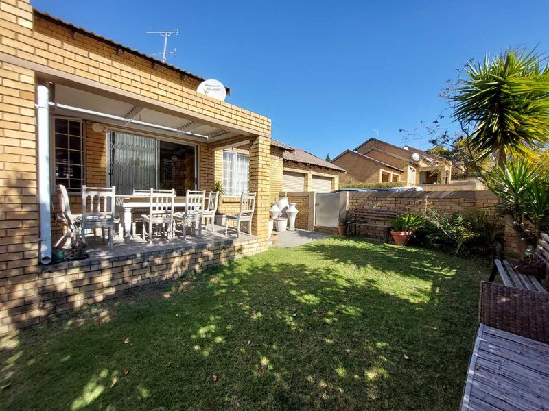 Rear view of the townhouse featuring a covered patio, brick facade, and a private garden area with boundary walling.