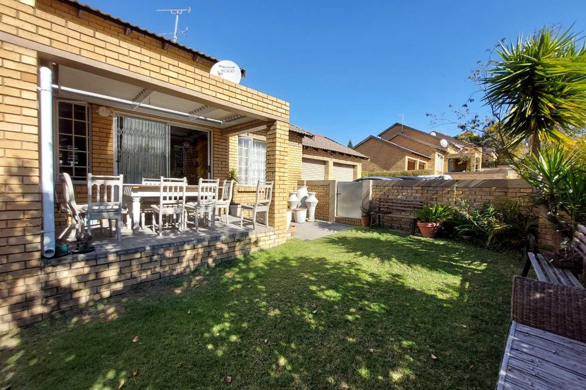 Rear view of the townhouse featuring a covered patio, brick facade, and a private garden area with boundary walling.