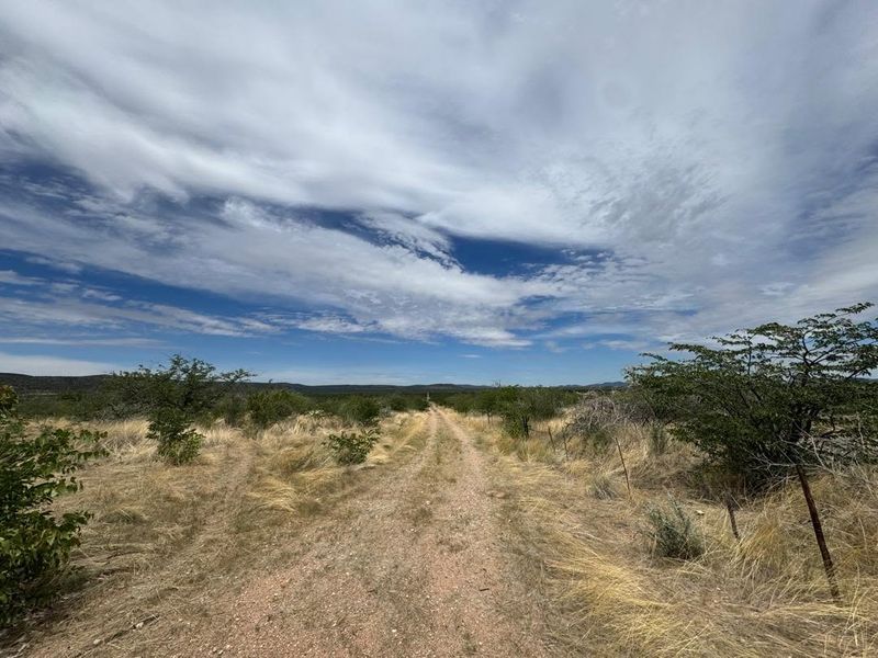 A wide-angle view of the farm landscape featuring a dirt access track and natural vegetation under a vast sky.