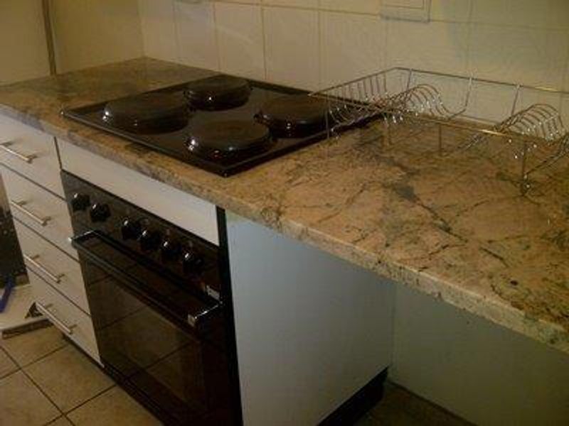 A kitchen area featuring a built-in oven, electric hob, and granite countertops with a tiled backsplash.