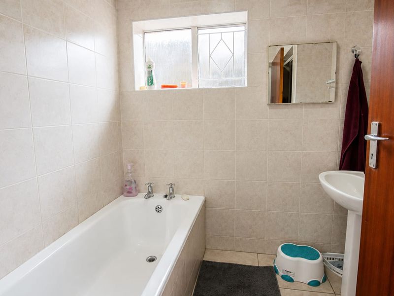 A functional bathroom featuring a bathtub, pedestal basin, and neutral wall tiling, providing a clean and practical space.