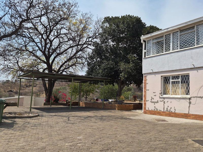 Rear exterior view showing a paved driveway, carport, and two-story building with visible wear to the exterior wall finishes.
