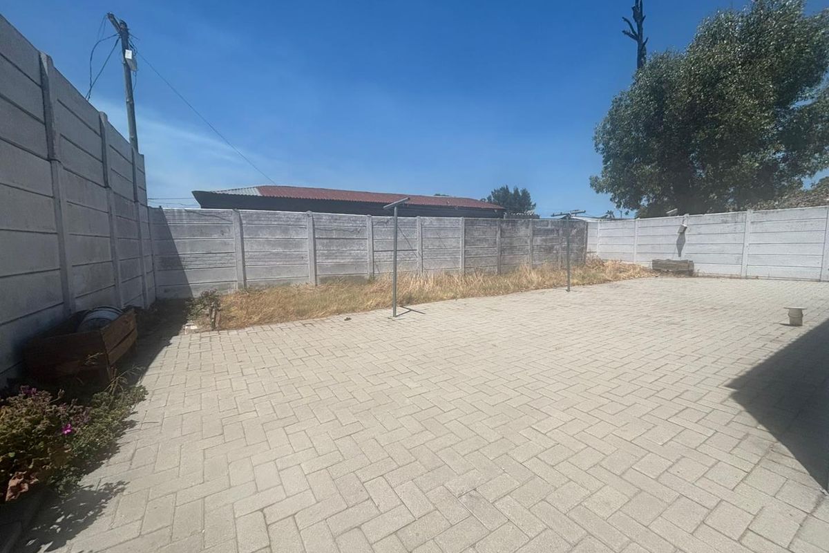 A paved rear courtyard area featuring concrete boundary walls and a clothesline, offering a functional outdoor space with potential for landscaping improvements.
