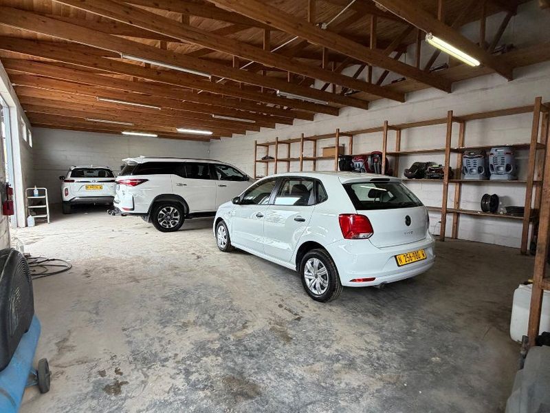 Spacious garage featuring exposed timber roof trusses, fluorescent lighting, and extensive built-in timber shelving units.