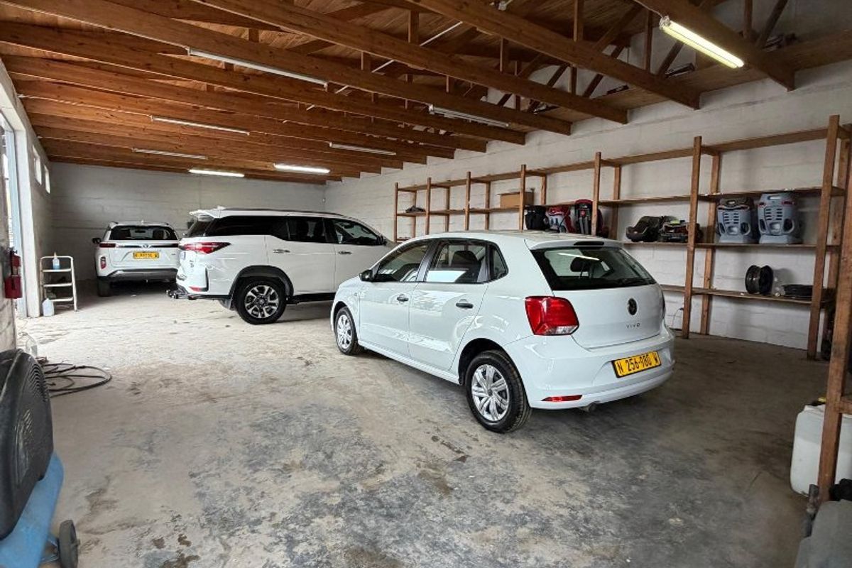 Spacious garage featuring exposed timber roof trusses, fluorescent lighting, and extensive built-in timber shelving units.